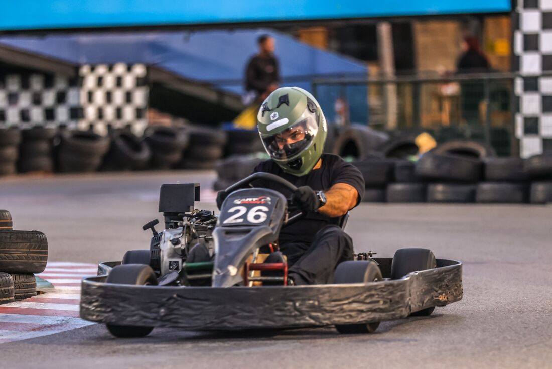 Piloto da comunidade Adrena no kart 26, com as bandeiras quadriculadas ao fundo