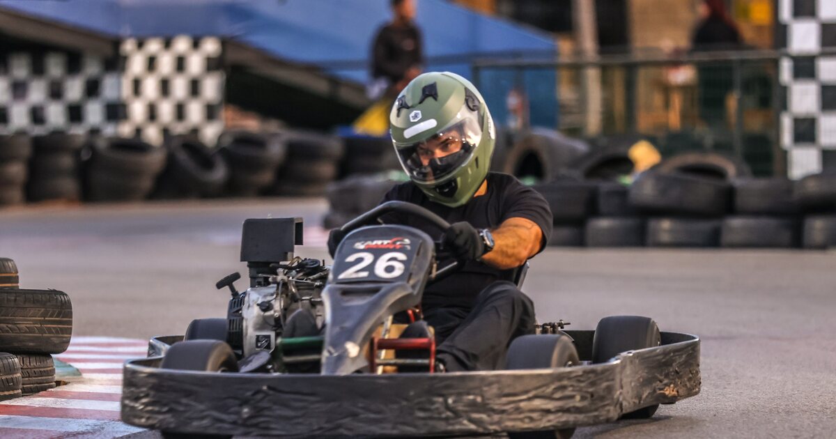 Piloto da comunidade Adrena no kart, com as bandeiras quadriculadas ao fundo